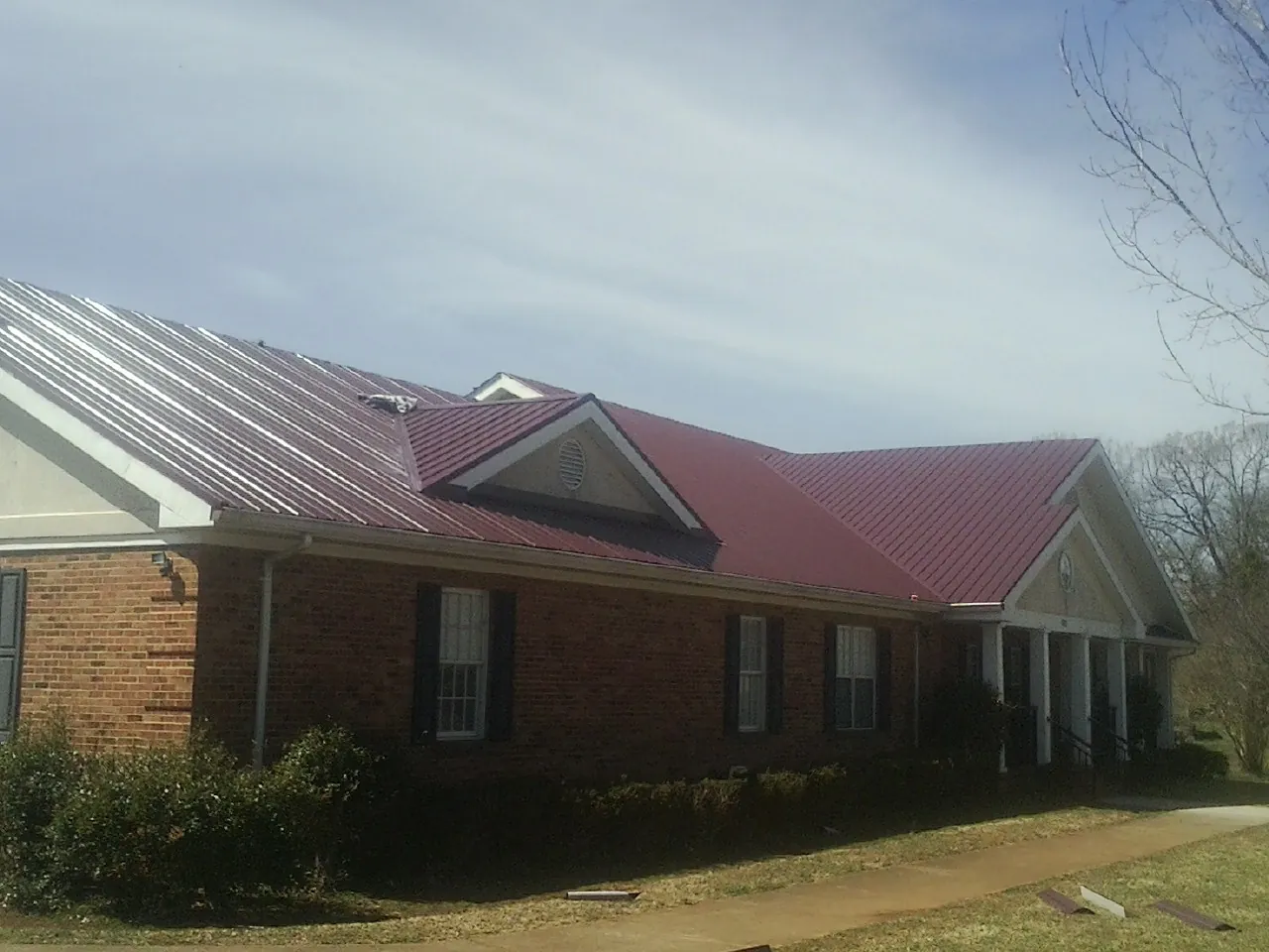 Red metal roof with gabled entries on a long brick building, from a Hail Damage Roof Repair job in Long Beach